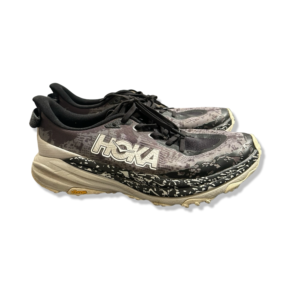 Svart och mönstrat par löparskor Hoka Speedgoat 6 för herr, fotograferade från sidan mot vit bakgrund.