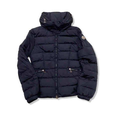 Blå dunjacka från Moncler för barn med hög krage och dragkedja, fotograferad framifrån mot en vit bakgrund.