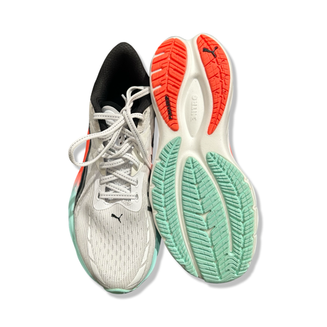 Ett par vita löparskor Puma Velocity Nitro 4 HYDROX för dam, visade uppifrån och med sulan vänd uppåt mot vit bakgrund.