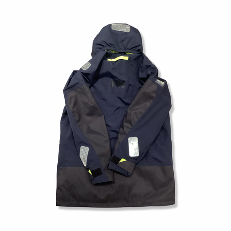 Baksidan av en blå Helly Hansen seglarjacka för dam med huva och reflexdetaljer, fotograferad mot en vit bakgrund.