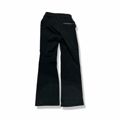 Baksidan av ett par svarta Peak Performance W Alpine Gore-Tex-skalbyxor för dam, fotograferade mot en vit bakgrund.