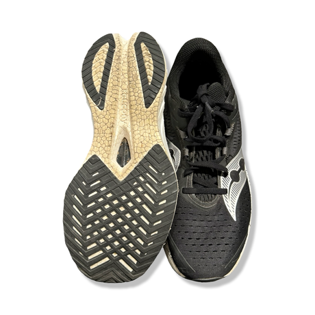 Svart par löparskor Saucony Endorphin Speed 4 för dam, visade uppifrån med sulan vänd uppåt mot vit bakgrund.