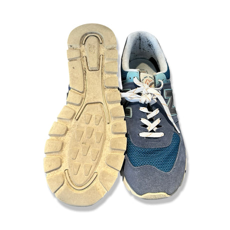 Blå New Balance sneakers för herr i mocka och mesh, fotograferade framifrån och med sulan uppåt.