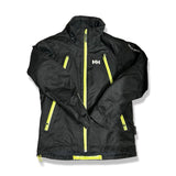 Svart skidjacka från Helly Hansen för barn i storlek 152, med gula dragkedjor, fotograferad framifrån mot en vit bakgrund.