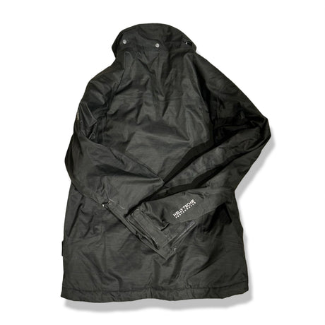 Baksidan av en svart skidjacka från Helly Hansen för barn i storlek 152, fotograferad mot vit bakgrund.