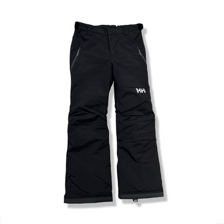 Svarta skidbyxor för barn från Helly Hansen med dragkedjefickor, fotograferade framifrån mot en vit bakgrund.