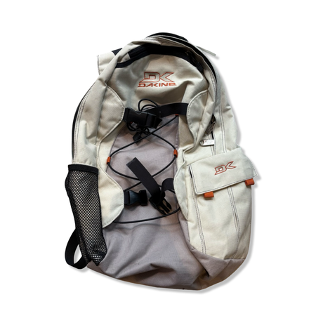 Beige Dakine-ryggsäck med grå detaljer, orange logotyp och svarta remmar, fotograferad mot vit bakgrund.