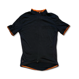 Triban svart kortärmad cykeltröja för dam med orangea detaljer och dragkedja, sedd framifrån mot en vit bakgrund.